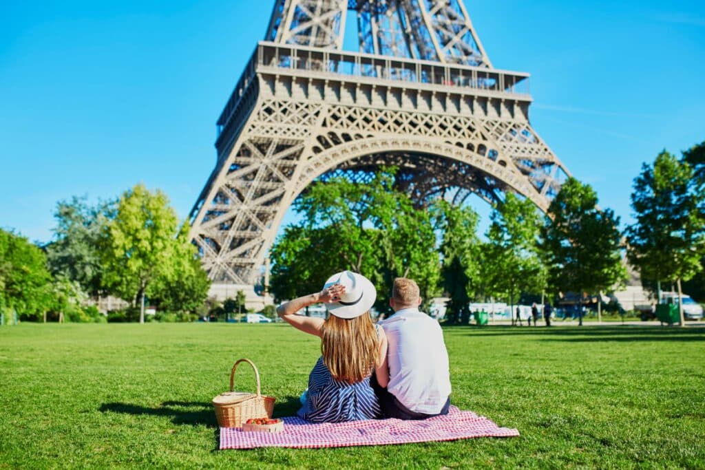 A couple sitting on grass with apicnic setup in front of the Eilffel tower