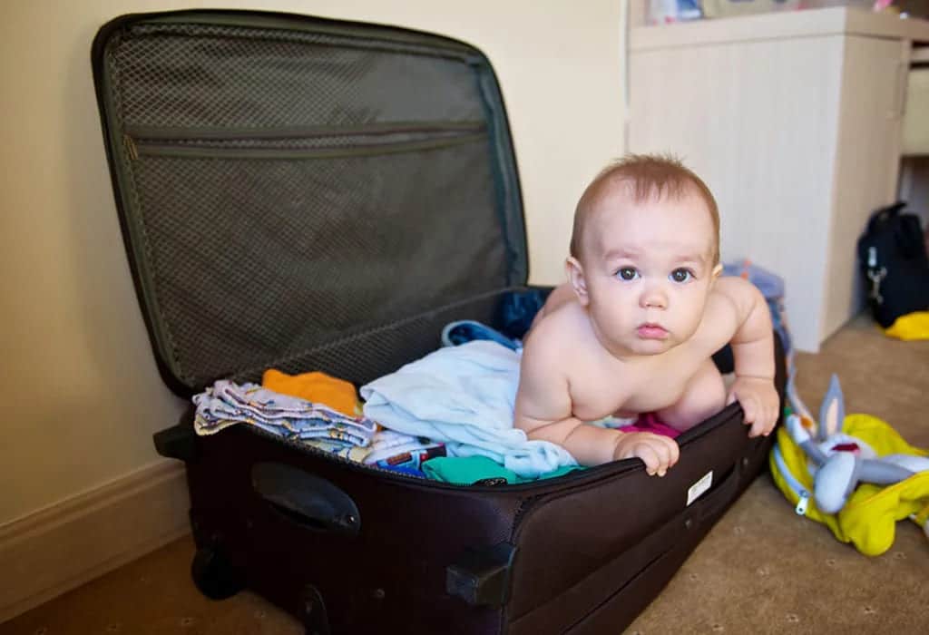 a toddler sitting a suitcase filled with clothes