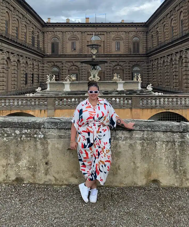 plus sized woman wearing floral jumpsuit pairing with sneakers standing infront of a historical building