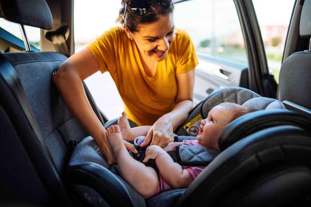 a mother adjusting a baby car seat while smiling at a baby