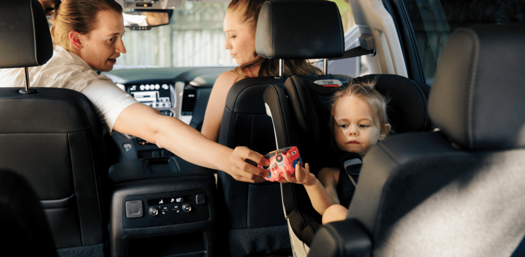 a mother is giving a toy to her daughter sitting in a car seat