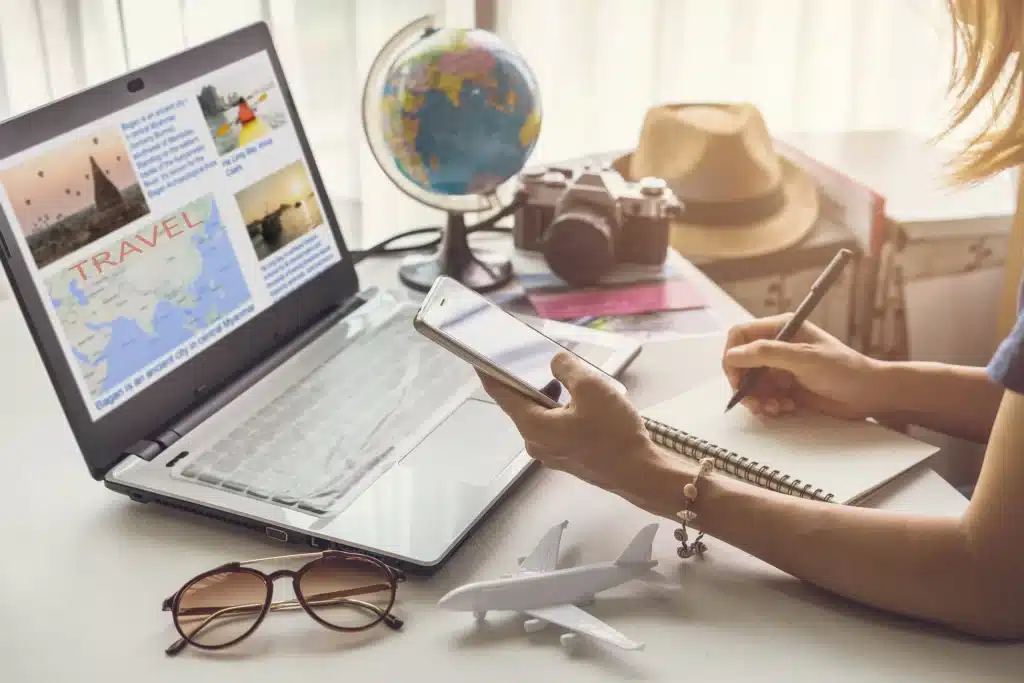 a women is using mobile phone and writting on a notepad and a latop and globe on a table