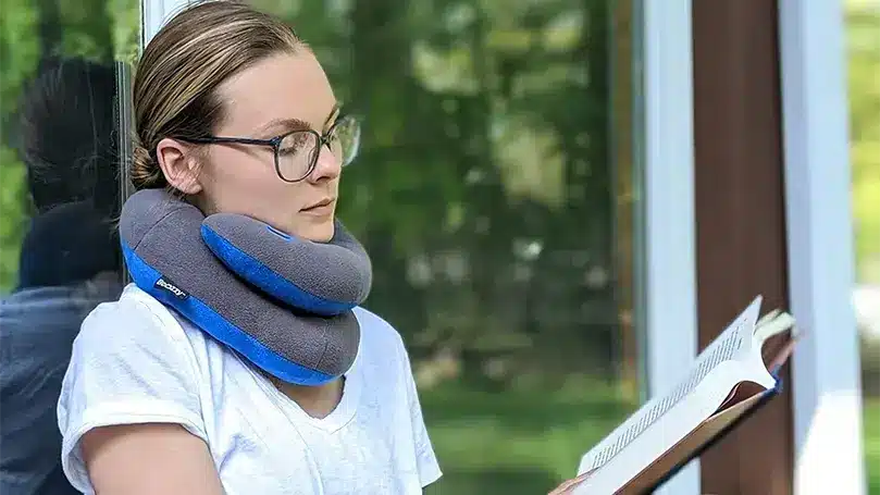 a woman reading a book while using Bcozzy Chin Supporting Travel pillow